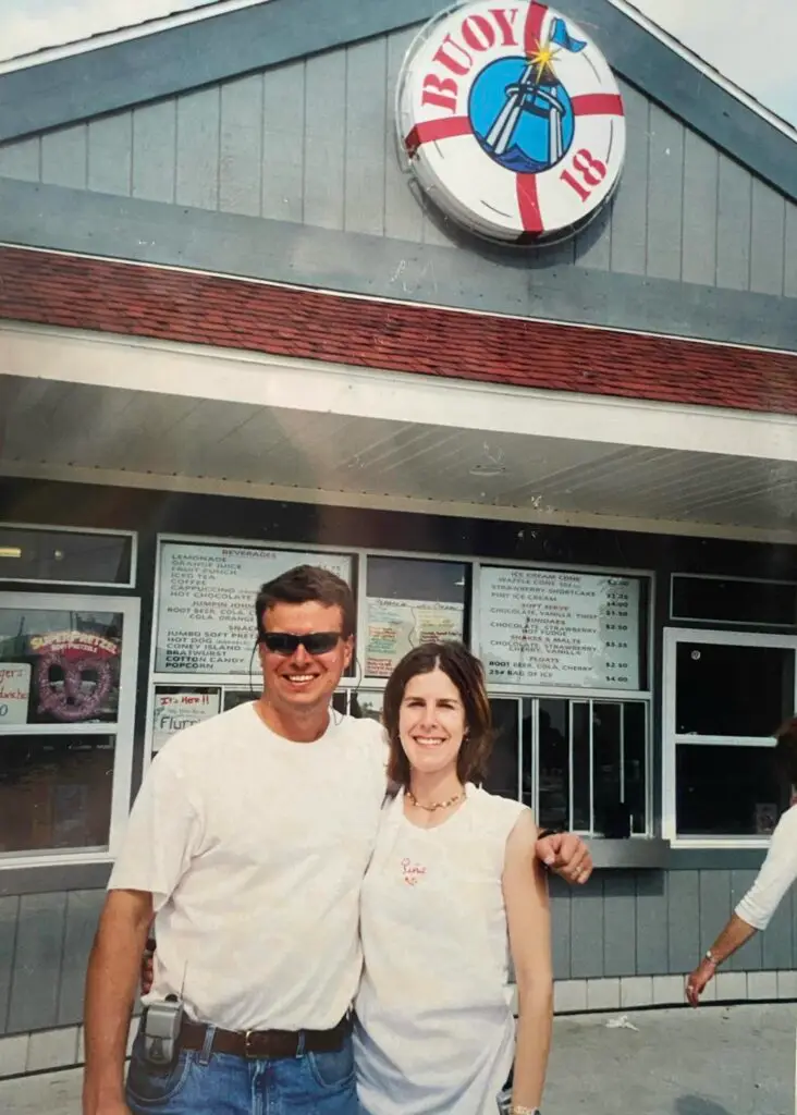 A historic photo of Tim and Jacqi Walli standing in front of the original Buoy 18 concession building beneath the iconic Buoy 18 sign.