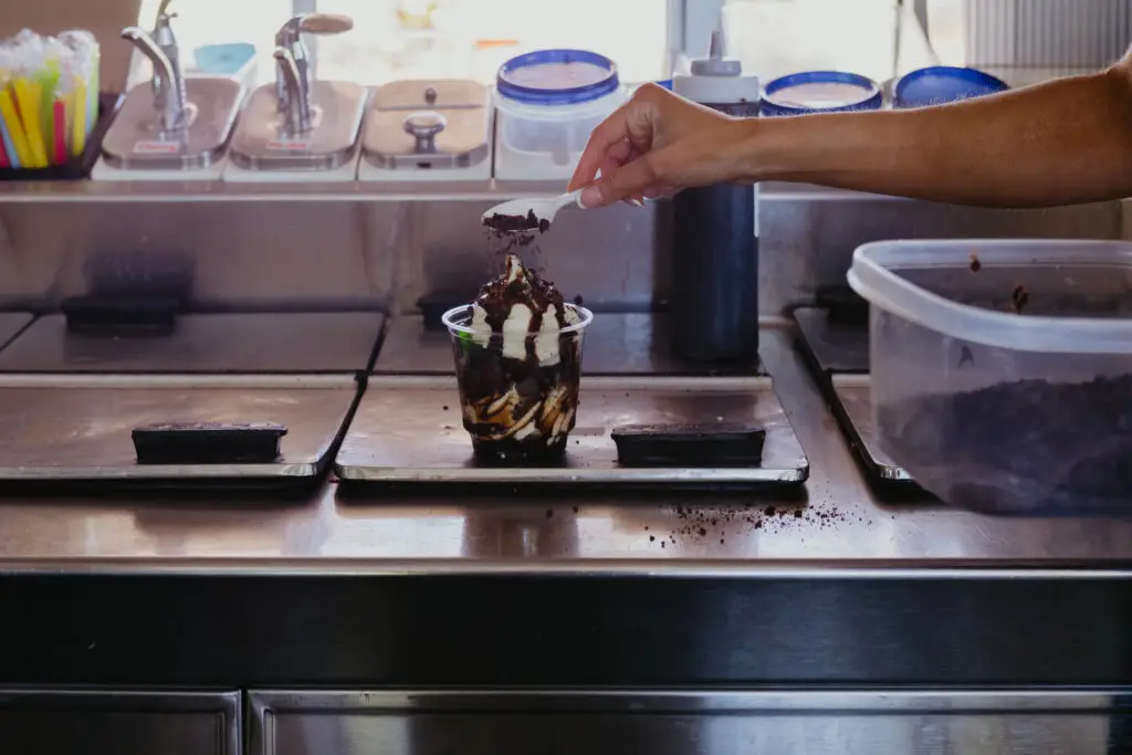 A chocolate ice cream sundae being topped with cookie crumbs and chocolate sauce at Buoy 18.
