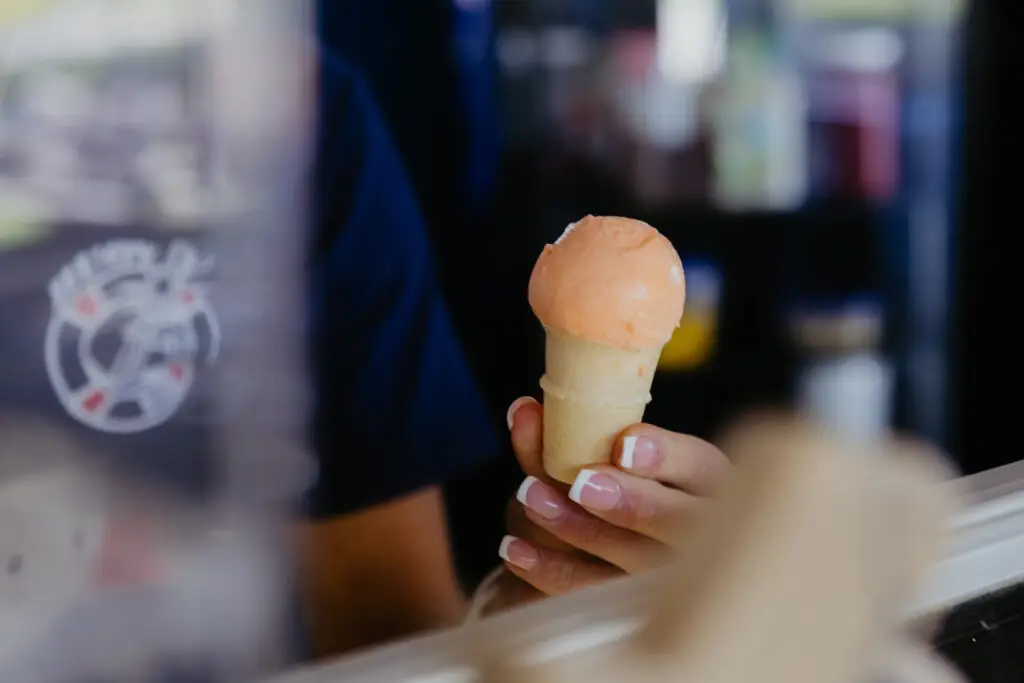 A freshly scooped orange ice cream cone being handed to a guest at Buoy 18.