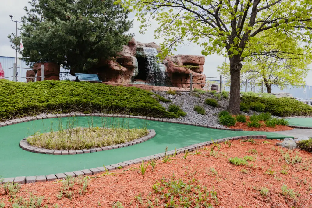 Scenic mini golf hole at Buoy 18 featuring a waterfall, landscaped greens, and mature trees in Bay City, Michigan.